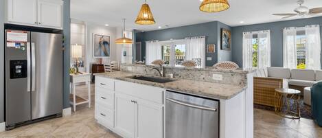 A modern kitchen with a stainless steel refrigerator, white cabinetry, a granite countertop, and a built-in dishwasher.