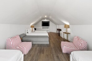 Ein Schlafzimmer im Loft-Stil mit schrägem Dach, einem Bett, einer Couch, zwei Sessel und einem kleinen Tisch mit Lampen.