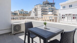 En balkon med bord og stole, en klimaanlæg og udsigt til et byggeplads med en kran.
