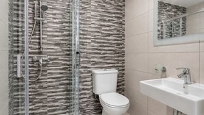 Et moderne badeværelse med bruseniche i glas, toilet og vask med spejl over.