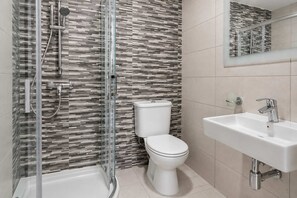 Un baño moderno con ducha envuelta en vidrio, inodoro y lavamanos con espejo.