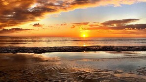Ein Sonnenuntergang über einem Strand, wobei Wellen den Himmel spiegeln.