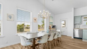 Una cocina moderna con comedor, que incluye una mesa de madera, sillas blancas y un candelabro.