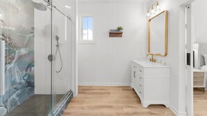 Ein modernes Badezimmer mit einer Duschkabine aus Glas, weißen Schränken und einem großen Spiegel.