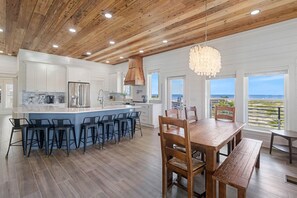 A modern kitchen with a central island, bar stools, and a dining area with a wooden table and chairs. - NEW HOME! AMISTAD IS AN UPSCALE 6BD/4BA HOME W/GULF & CANAL VIEWS, PRIVATE POOL! (Mexico Beach)