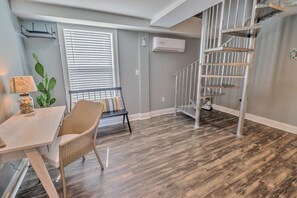 Ein Zimmer mit Esstisch, Korbsessel, einer Bank mit Streifenpolster, einer Treppe und einer Klimaanlage.