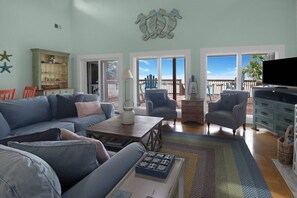 A living room with a sofa, armchairs, a coffee table, and a television. There are windows with a view of the outdoors. - CABANA DEL SOL IS A 2BD/2BA GULF FRONT W/AMAZING VIEWS, 2 SCREEN PORCHES! (Port Saint Joe)