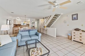 A modern living room with a sofa, coffee table, and a staircase leading to an upper level. - Cape it Simple -  OFFERS GULF VIEWS & STEPS TO THE BEACH! COMMUNITY POOLS! (Port Saint Joe)