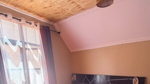 Una camera da letto con soffitto in legno, un letto con copripiumino a righe rosse e bianche, una testata nera e un lampadario.