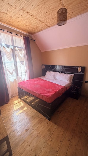 Un dormitorio con techo de madera, una cama con colcha a rayas rojas y blancas, cabecera negra y una lámpara colgante.