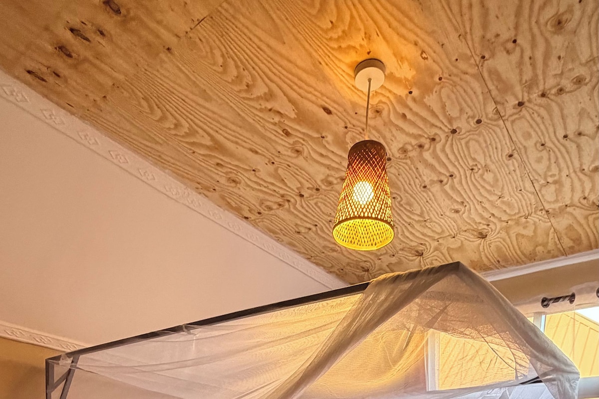 Una cama de madera con dosel, ropa de cama blanca y una colcha roja estampada.