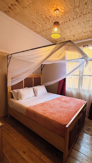 Una cama de madera con dosel, ropa de cama blanca y una colcha roja estampada.