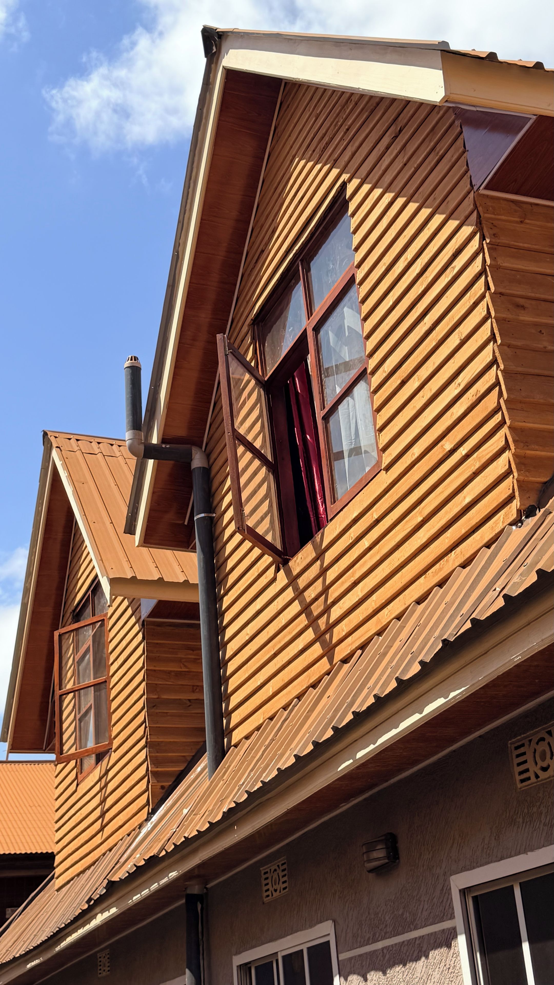 Un edificio de madera con techo inclinado, una chimenea y una ventana con cortina roja.