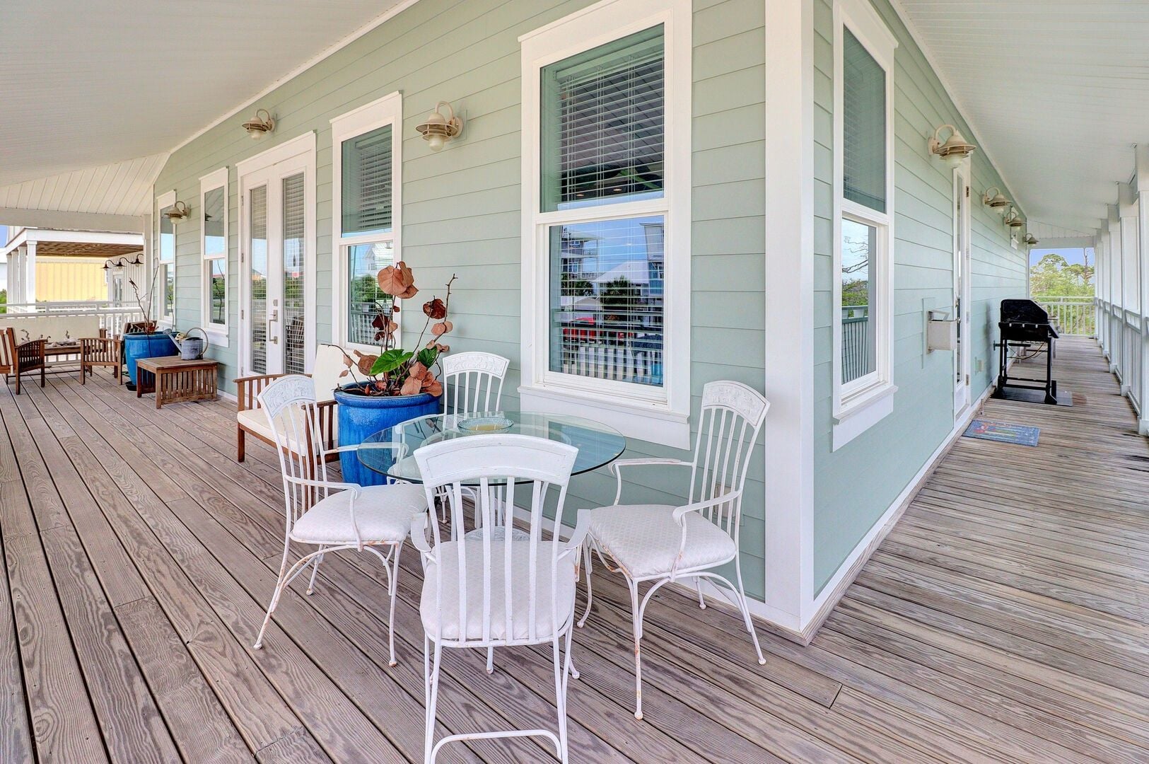 A covered porch with a table and chairs, a grill, and a potted plant.