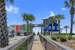 A wooden boardwalk leading to colorful beach houses with a sign indicating 'Ocean Harbor.' - Carpe Diem,  A Luxury Home With Amazing Gulf Views Views, Fire Pit, Pet-Friendly (Port Saint Joe)