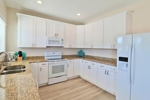 A kitchen with white cabinets, a stainless steel sink, a microwave, a stove, and a refrigerator. - THIS DUPLEX IS PERFECT FOR LARGE FAMILIES/ MULIIPLE FAMILES! STEPS AWAY FROM THE (Mexico Beach)