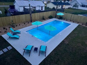 Una piscina rectangular amb una terrassa enrajolada, envoltada per una tanca de fusta.