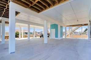 A spacious covered area with concrete flooring and white pillars, featuring a staircase and a view of the surrounding landscape. - THE "CRABBY HUNTER" IS A NEW HOME W/GULF VIEWS, PRIVATE POOL & OPTION TO RENT GO (Mexico Beach)