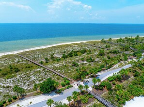 An aerial view of a coastal area with a paved walkway, palm trees, and a beach. - Cypress Sunshine is a 4BD/2BA home steps from north pool & beach boardwalk! Rent (Port Saint Joe)