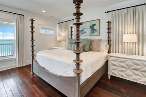 A four-poster bed with a textured white bedspread, a nightstand with a geometric-patterned drawer, and a painting on the wall. - ENDLESS SUMMER  IS A LUXURIOUS, CUSTOM GULF FRONT HOME, WITH PANARAMIC VIEWS! (Port Saint Joe)