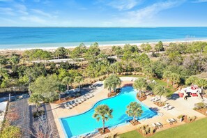 Ett semesterhotell med en swimmingpool, solstolar och utsikt över stranden och havet.