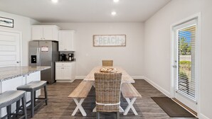 Eine Küche mit weißen Schränken, einem Edelstahlkühlschrank, einem Holztisch mit Bänken und einem Schild an der Wand mit der Aufschrift 'BEACH'.