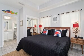 A hotel room with a large bed, a bedside table with a lamp, a mirror, and a view of the bathroom. - "Georgia Sand" is 600 steps to the beach! This 2BD/2BA adorable cottage sleeps 8 (Mexico Beach)