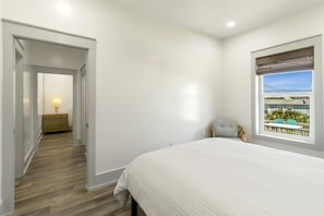 A bedroom with a bed, a chair, a window with a view, and a door leading to another room. - NEW LISTING! Grand Coral, a 4BD/2BA luxury home with a living/kitchen/dining are (Mexico Beach)