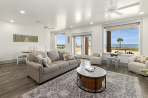 A spacious living room with a large sofa, a coffee table, and a view of the beach. - New Listing, Grand Coral II has gulf views & 100 steps to the beach! 2BD/1BA lux (Mexico Beach)