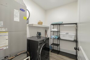 A laundry room with a washing machine, dryer, and shelves for laundry. - New Listing, Grand Coral III has gulf views & 100 steps to the beach! 2BD/1BA lu (Mexico Beach)