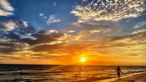 Ein Strand mit Sonnenuntergang, Wellen und einer Person, die spazieren geht.