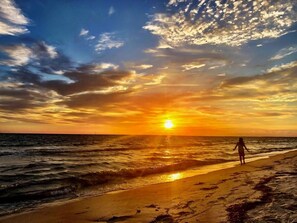 En strand med en solnedgång, vågor och en person som promenerar.