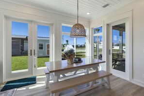 A dining area with a wooden bench, a hanging light fixture, and a view of a grassy yard through large glass doors. - La Buena Vida is a 3BD/3BA, newly built home w/modern amenities, screened-in por (Mexico Beach)
