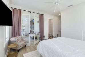 A bedroom with a bed, a chair, a TV, and a door leading to a bathroom. - La Buena Vida is a 3BD/3BA, newly built home w/modern amenities, screened-in por (Mexico Beach)