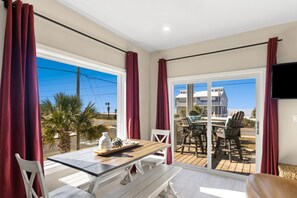 Ein Zimmer mit Tisch und Stühlen, einem Fenster mit Vorhängen und Blick auf ein Gebäude.