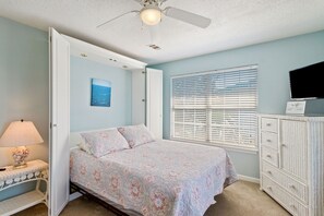 Ein Schlafzimmer mit einem Bett, einem Nachttisch, einer Kommode, einem Deckenventilator und einem Fenster mit Jalousien.