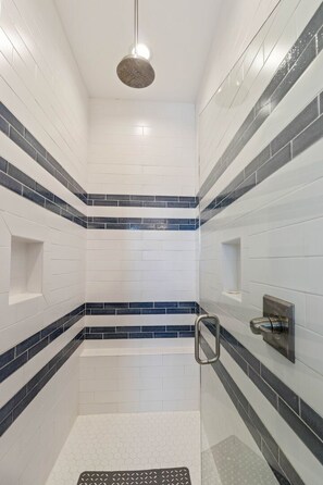 A shower with white and dark blue tiles, a metal showerhead, and a handrail. - Oak Rest Barn, is a custom built gulf front home w/pool, pet friendly, $250 cred (Port Saint Joe)
