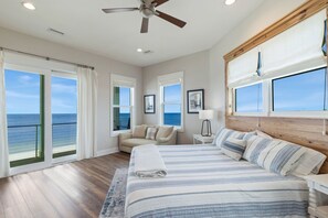 A bedroom with a large bed, a ceiling fan, and a view of the ocean through large windows. - Oak Rest Barn, is a custom built gulf front home w/pool, pet friendly, $250 cred (Port Saint Joe)