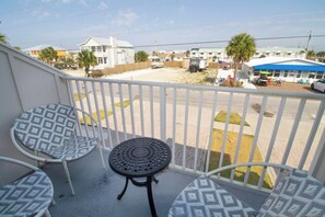 A balcony with two patterned chairs and a small table, overlooking a street with buildings and a beach. - PEACEFUL EASY FEEELING OFFERS GULF VIEWS & STEPS FROM BEACH! COMMUNITY POOL! (Mexico Beach)