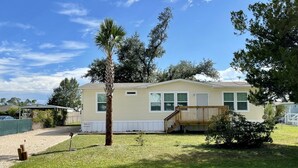 A single-story mobile home with a covered porch, a small lawn, and a palm tree. - PETE'S PARADISE IS MODERN, SPACIOUS FLOOR PLAN! GREAT FENCED IN BACKYARD WITH FI (Port Saint Joe)