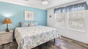 A bedroom with a bed, a nightstand, a lamp, a framed picture, and a window with blinds. - PETE'S PARADISE IS MODERN, SPACIOUS FLOOR PLAN! GREAT FENCED IN BACKYARD WITH FI (Port Saint Joe)