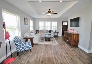 A living room with a sectional sofa, a coffee table, a side table, a floor lamp, and a TV mounted on the wall. - PINK FLAMINGO, 3BD/2BA W/FENCED IN BACKYARD IN QUIET NEIGHBORHOOD! COMMUNITY POO (Mexico Beach)