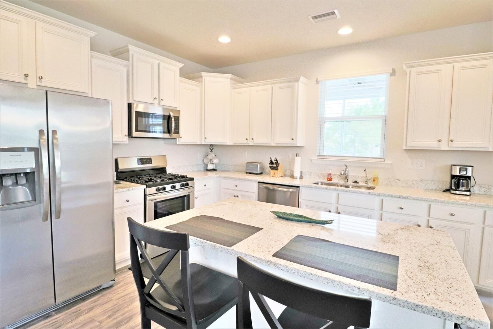 A modern kitchen with white cabinetry, stainless steel appliances, and a central island with seating.