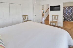 A bedroom with a large bed, two wooden chairs, a TV on the wall, and a staircase leading to another room. - RAY'S ROOST WITH 6BD, 2 FULL KITCHENS, 2 LIVING AREAS, PERFECT FOR MULTI FAMILIE (Mexico Beach)