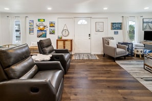 A living room with leather sofas, a television, and various wall decorations. - "Recuperation Cottage" offers gulf views and is steps to the beach! Pet-friendly (Port Saint Joe)