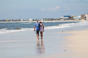 A couple walking on a beach with a view of the ocean and buildings in the background. - "Recuperation Cottage" offers gulf views and is steps to the beach! Pet-friendly (Port Saint Joe)