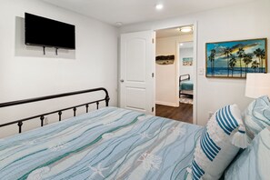 A bedroom with a bed, a television on the wall, a door leading to another room, and a painting on the wall. - "Recuperation Cottage" offers gulf views and is steps to the beach! Pet-friendly (Port Saint Joe)