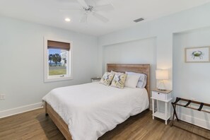 A bedroom with a bed, a nightstand, a ceiling fan, a window with a view, and a framed picture on the wall. - "Salt Therapy" offers gulf views, 100 steps to beach, modern 2BD/2BA, single lev (Port Saint Joe)