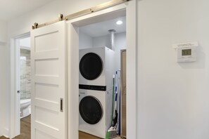 A laundry room with two stacked washing machines, a wall-mounted thermostat, and a door leading to another room. - "Salt Therapy" offers gulf views, 100 steps to beach, modern 2BD/2BA, single lev (Port Saint Joe)