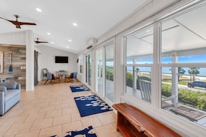 A spacious living area with a large window, a ceiling fan, and a wooden bench. - "SALT WIND" HAS GULF VIEWS, STEPS TO BEACH, SECLUDED & PEACEFUL! (Mexico Beach)